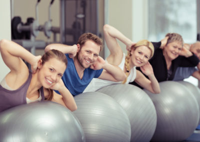 un groupe de personnes de tous âges pratique le Pilates avec de gros ballons