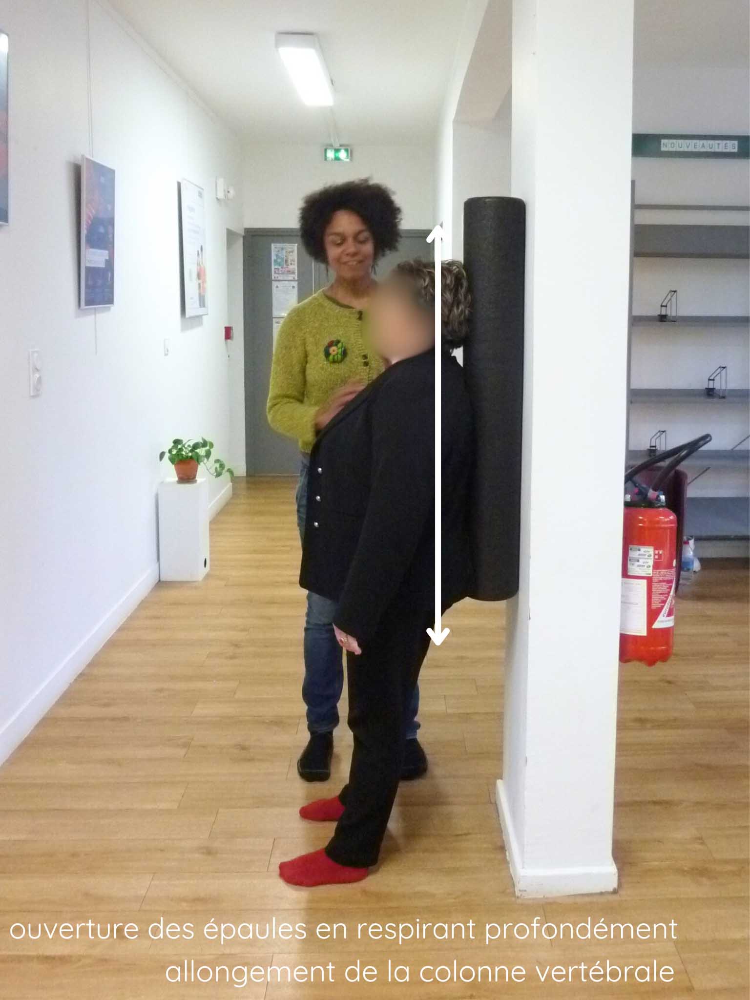 rouleau-1 Une personne est appuyée contre un rouleau de Pilates qui est contre un mur. Des flèches (une vers le haut vers la tête, l'autre vers le bas vers le sacrum) indiquent le mouvement à faire pour étirer son dos. Une indication est mentionnée sur la photo : ouverture des épaules en respirant profondément et allongement de la colonne vertébrale